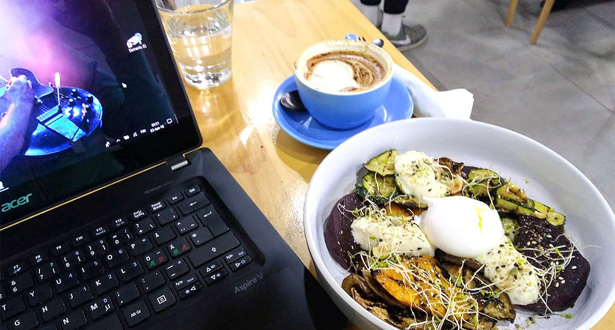 Cup of coffee, glass of water, and a vegetarian meal next to a black laptop.